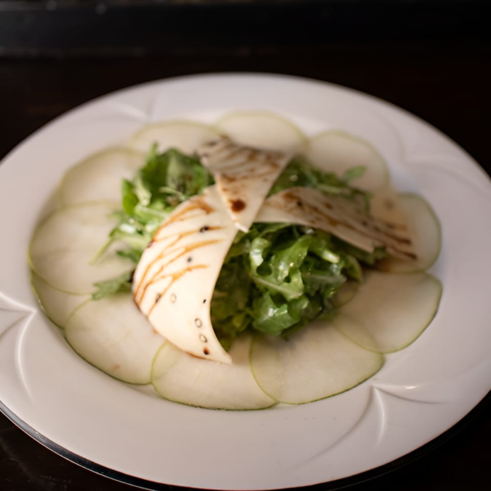 A white plate with thinly sliced green apples, arugula salad, and grilled halloumi cheese.