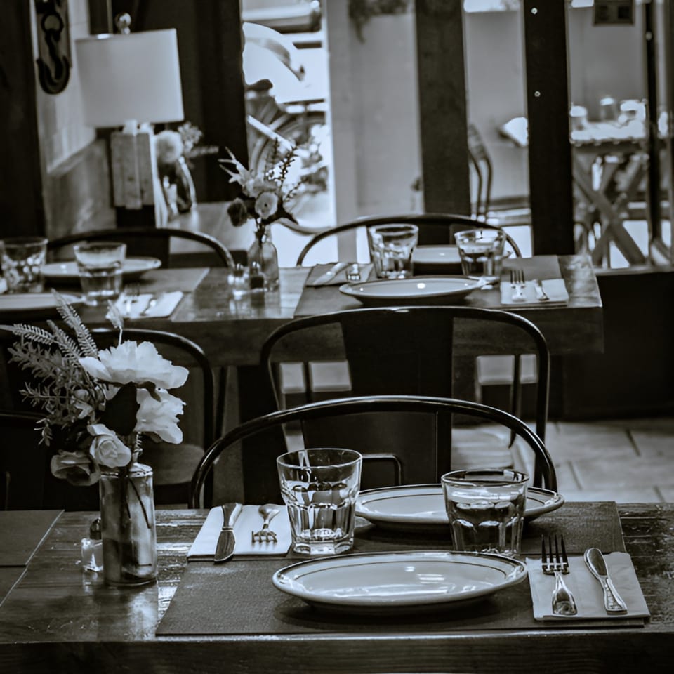 Black and white photo of set tables with plates, glasses, and floral centerpieces inside Porto Salvo.