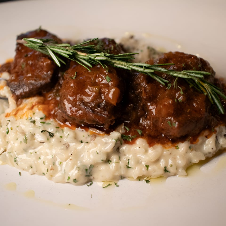 Braised short ribs in a rich sauce, served over creamy risotto and garnished with rosemary.