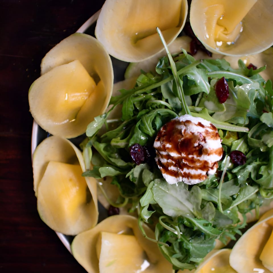 Italian dish with tortellini, arugula, cranberries, and a dollop of cheese with balsamic glaze.