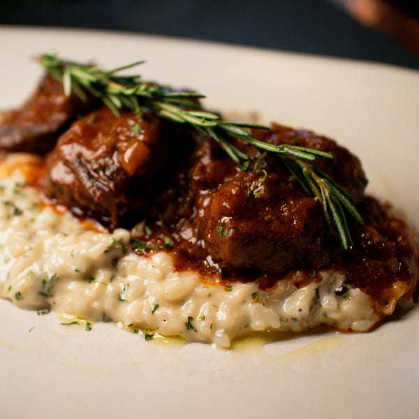 Braised short ribs in a rich red sauce, served over creamy risotto and garnished with rosemary.