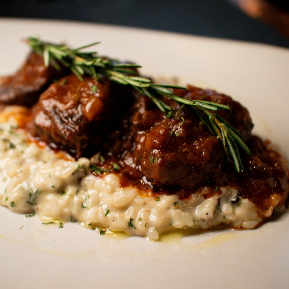Braised short ribs in a rich red sauce, served over creamy risotto and garnished with rosemary.