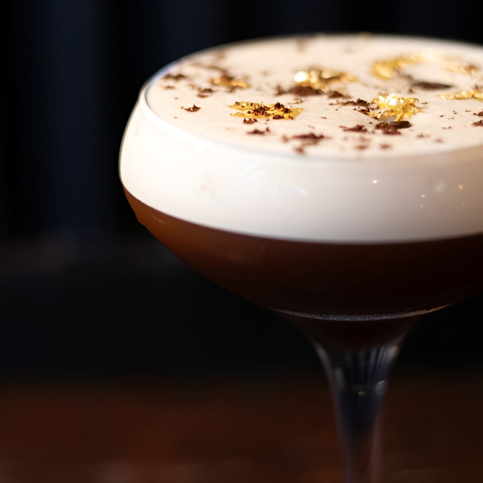 Espresso martini with a foamy top, garnished with gold flakes and coffee grounds.