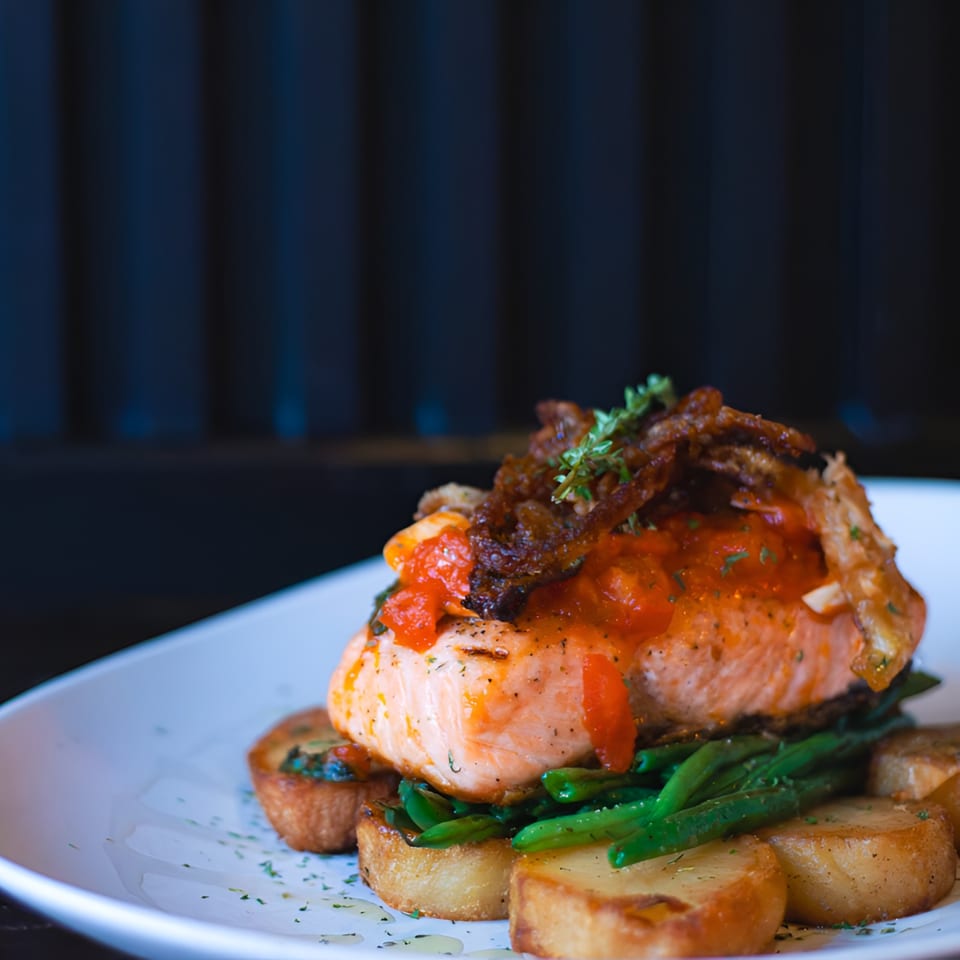 Porto Salvo's salmon dish with tomato sauce, green beans, and roasted potatoes on a white plate.