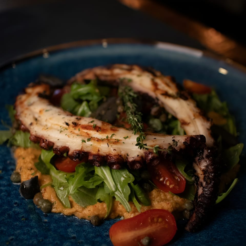 Grilled octopus with arugula, cherry tomatoes, and capers on a blue plate at Porto Salvo.