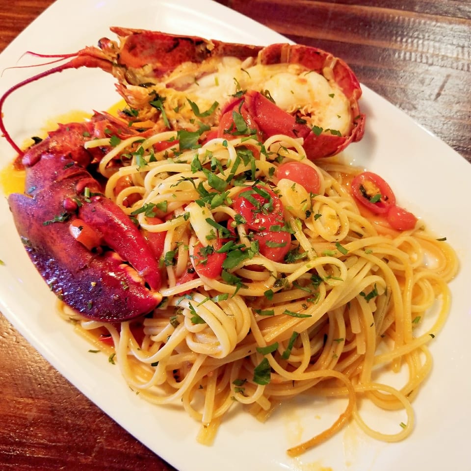 Porto Salvo's linguine pasta with lobster, cherry tomatoes, and fresh parsley on a white plate.